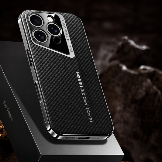 A black case with diagonal carbon-fiber-style lines stands on an angular dark pedestal among rough rocks. Its silver border follows the slanted three-lens camera surround.