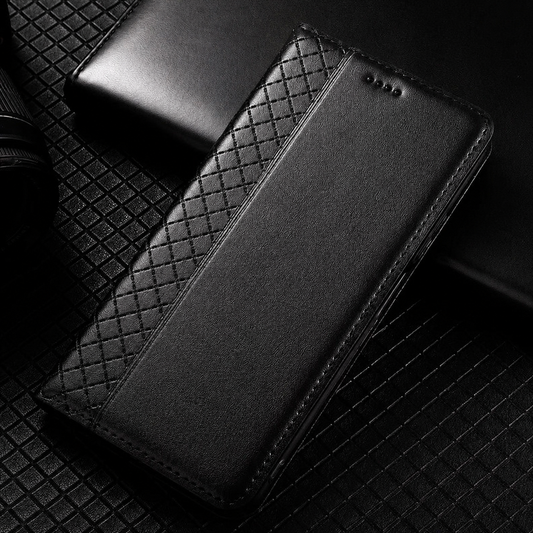 A closed black flip phone wallet lies diagonally on a black textured surface beside a smooth black cover. A narrow strip of crisscross diamond texture runs along its fold, contrasting with the smooth front panel. Stitching outlines the rounded edges, and four small earpiece holes sit near the top.
