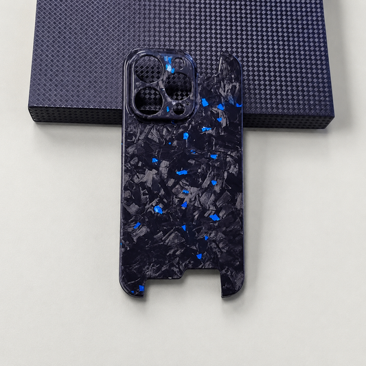 A glossy black phone case with blue and gray shard-like flecks rests beneath a dark textured box, showing circular camera openings and open sections at both ends.