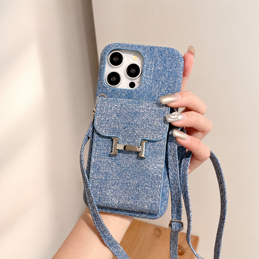 A hand holds a blue woven-textured case against a softly lit beige background. Its rear flap pocket has a silver H-shaped clasp and matching cord straps.