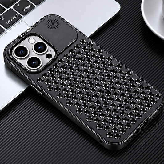 A black perforated phone case lies diagonally beside a laptop keyboard and cup on ridged black material. Rows of circular three-spoke openings cover its back below the camera panel.
