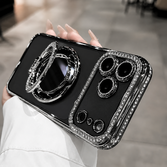 A hand holds a black reflective case with silver-colored rhinestone trim and individual camera rings. A circular mirror grip is opened outward from the back.