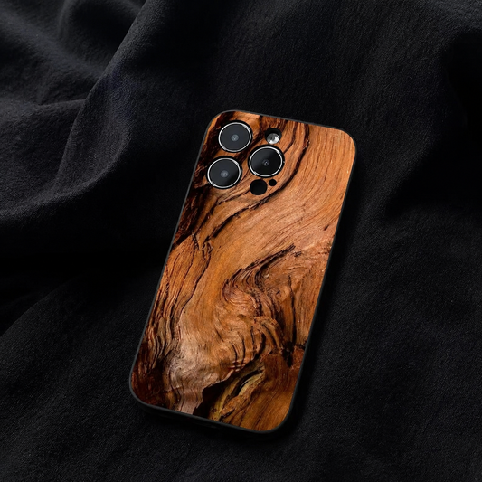 A warm brown wood-grain phone case rests on folded black fabric. Broad swirling grain and dark knots cross its back beneath three individual camera openings.