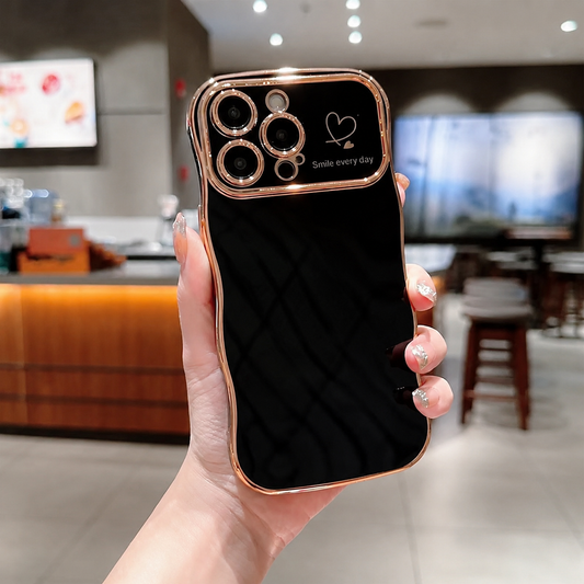 A hand holds a glossy black case in a café, with wavy rose-gold-colored edging, camera lens rims and a small heart above 'Smile every day'.