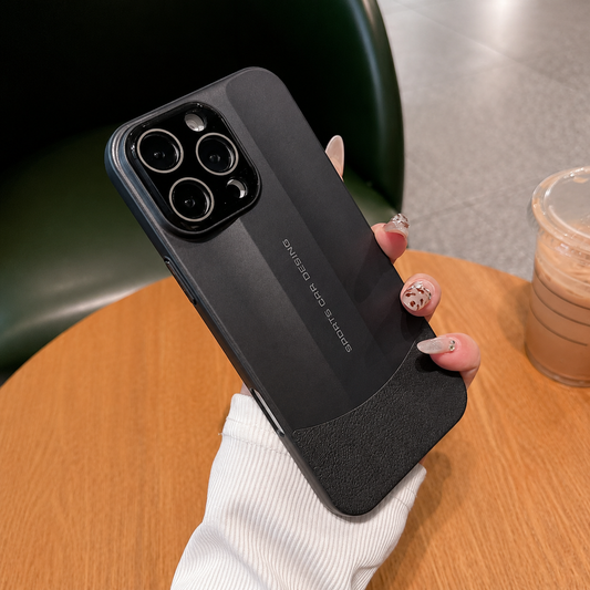 A hand holds a dark gray phone case above a wooden cafe table beside an iced drink, showing its angular back panel and black three-lens camera panel.