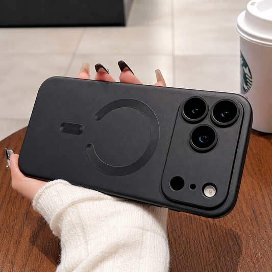 A hand holds a charcoal phone case horizontally above a wooden table, with a broad camera guard and open circular back ring.