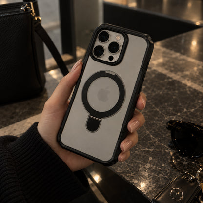 A hand holding a phone case with a black MagSafe ring on a light gray back, set against a dark marble countertop with a black handbag and sunglasses in the background.