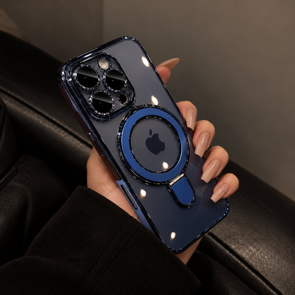 A hand holding a dark blue glossy magnetic phone case with a raised circular MagSafe ring and a small kickstand, shown against a dark leather seat background.