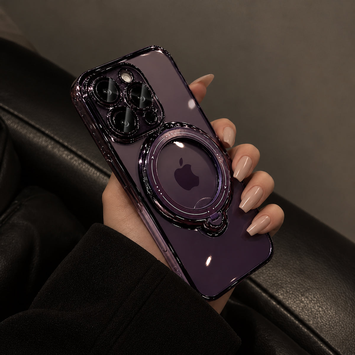 A hand holding a dark purple iPhone case with a built-in kickstand and MagSafe ring, resting on a black leather surface.