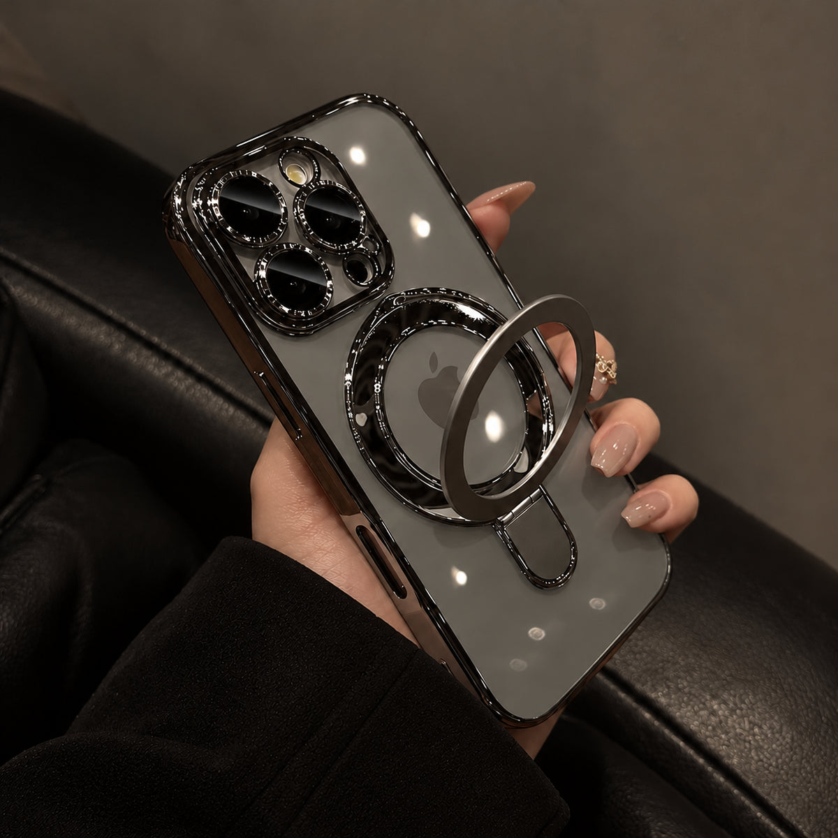 A hand holding a smartphone case with a large circular ring stand and a metallic camera border, shown against a dark leather seat background.