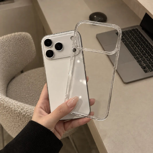 A hand holds a clear, transparent phone case over a white smartphone, with a desk, laptop, and chair visible in the background.