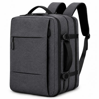 A charcoal gray rectangular backpack stands at an angle with a front zipper pocket, top handle, padded straps, side handle and compression buckles.