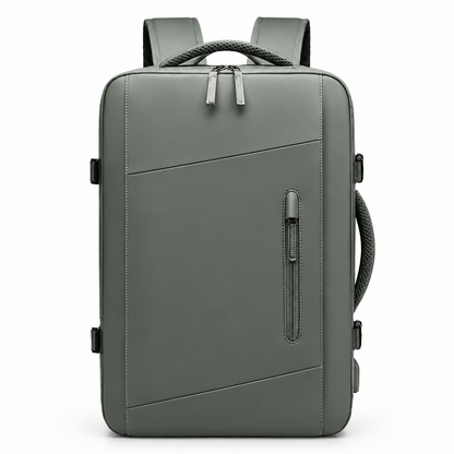 A gray-green rectangular backpack faces forward, showing diagonal front seams, a narrow vertical zip pocket, double main zipper, woven top and side handles and padded shoulder straps.