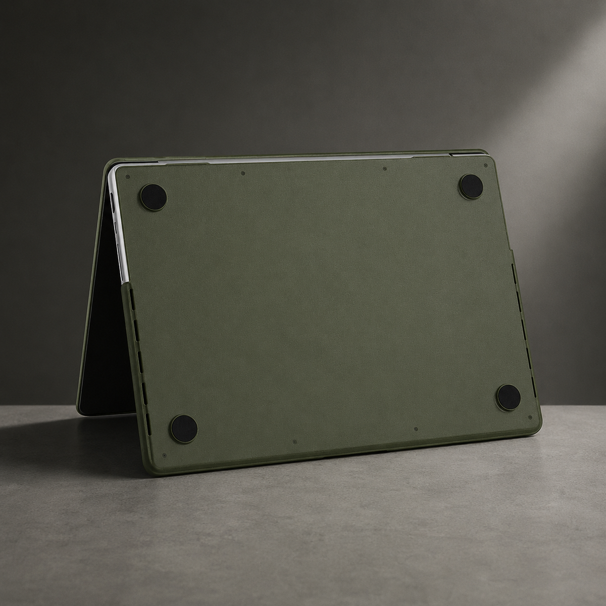 An olive green-covered MacBook stands partly open in a tent position, showing its underside with four round black corner feet and fitted edge clips.