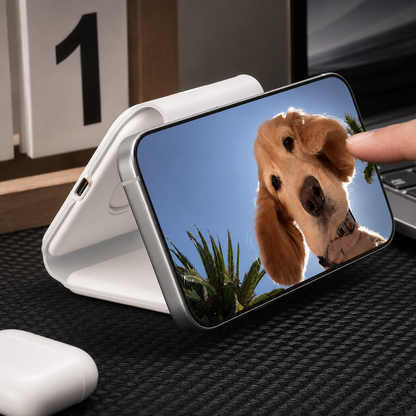 A hand touches a horizontal phone displaying a golden dog's face, supported by a white charger folded into a triangular stand.