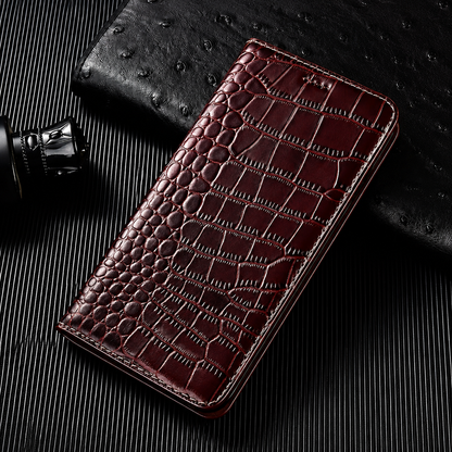 A closed burgundy flip wallet lies diagonally on a dark ribbed surface beside a textured black accessory and small bottle. Its glossy crocodile-like pattern has rounded scales along the fold and larger rectangular scales across the cover. Matching stitches outline the rounded edges.
