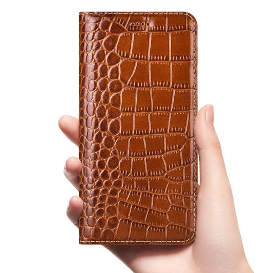 A hand holds a closed tan flip wallet upright on white. A glossy crocodile-like pattern combines small rounded scales near the fold with broad rectangular scales across the cover. Matching stitching outlines the edge, with small earpiece holes near the top.