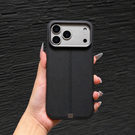 A hand holds a black stitched case against a dark textured wall. Its narrow central seam and small metallic tab contrast with the plain back.