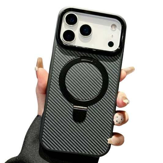 Hand holds a black-edged case upright against white. Its back has a diagonal carbon-fiber-style weave and a large glossy black circular ring stand folded flat below the camera opening.