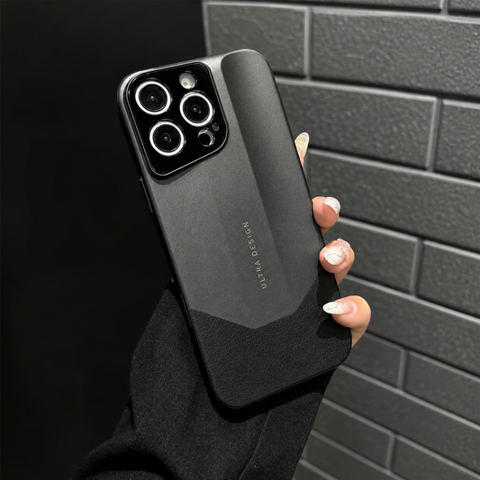 A hand in a black sleeve holds a dark gray phone case beside a black brick wall. An angular raised back panel meets a darker lower section below the camera panel.