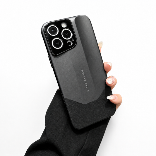 A hand in a black sleeve holds a dark gray phone case against white. Its angular raised back panel contrasts with a darker lower section beneath a black three-lens camera panel.