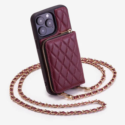 Burgundy quilted phone wallet case stands upright with a raised zippered pocket and black border. A gold-colored chain woven with burgundy material loops around it.