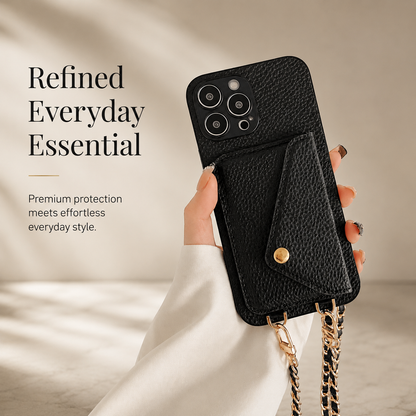 Hand holds a black pebbled phone wallet upright on beige. Its envelope-shaped rear pocket is fastened with a gold-colored snap, and a woven chain hangs below.