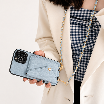 A woman holds a pale blue pebbled phone wallet horizontally while wearing its woven chain. The envelope-shaped rear pocket is fastened with a small gold-colored snap.