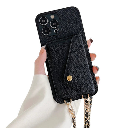 Hand holds a black pebbled leather-look case with an envelope-shaped rear card pocket and gold-colored snap. A woven gold-colored chain hangs from two clips at the bottom.