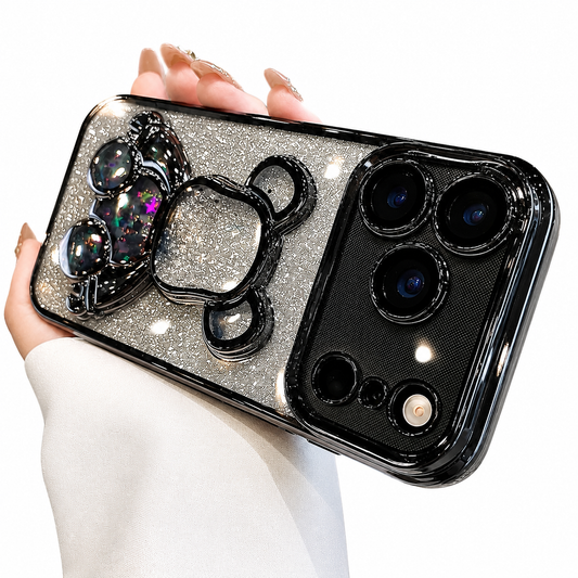 A hand holds a silver-glitter case horizontally against white, with black glossy camera trim and a bear-shaped decoration containing colorful star-like glitter in clear compartments.