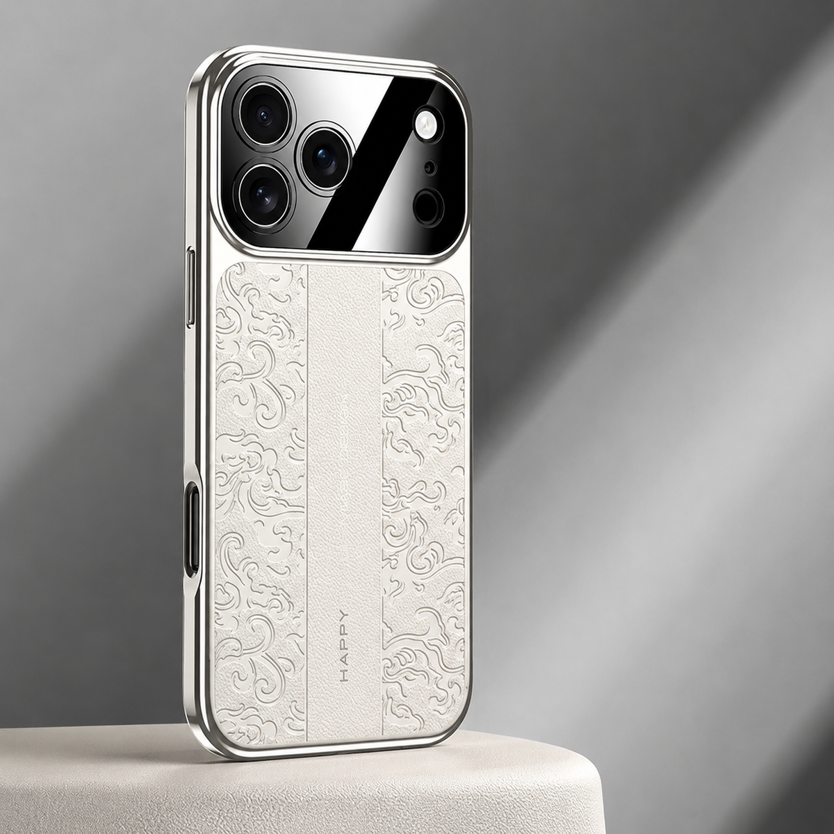 A cream-white embossed case stands on a pale pedestal. Silver-looking sides border the curling motifs and plain central strip below a reflective camera panel.