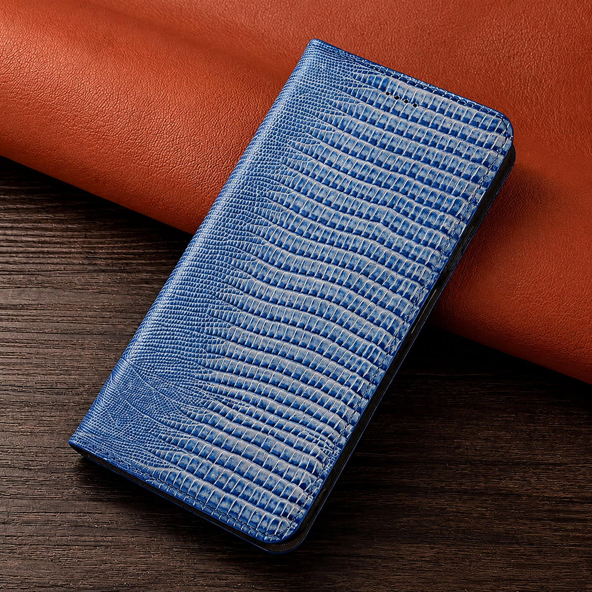 A closed blue reptile-patterned folio case leans against orange material on a dark wooden table.
