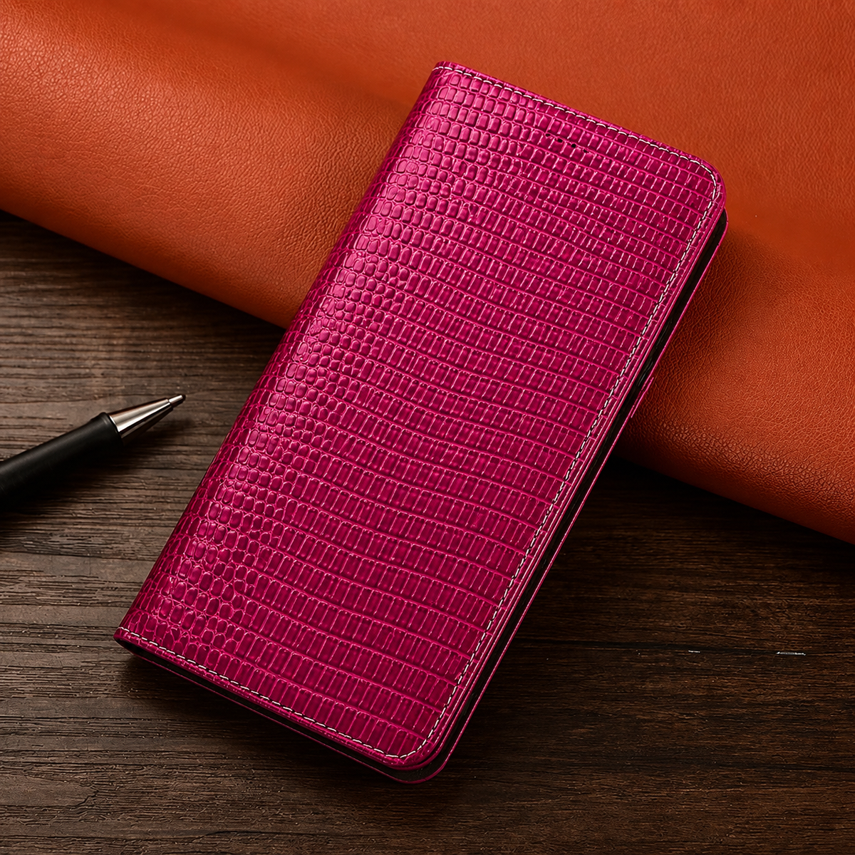A closed bright pink reptile-patterned folio case lies near a pen on a dark wooden table.