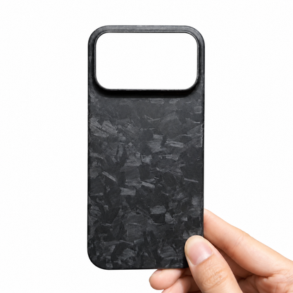 A hand holds a black phone case against white. Irregular gray shard-like patches cover its back below a wide rectangular camera opening.
