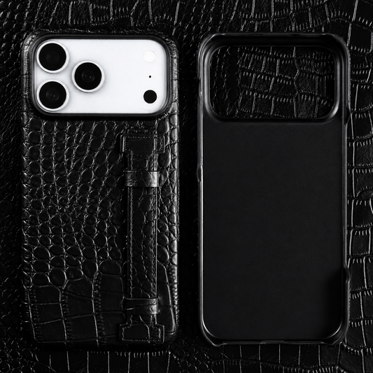 A black textured case and empty matching shell lie on black crocodile-patterned material. A vertical stitched strap sits along the case's back.
