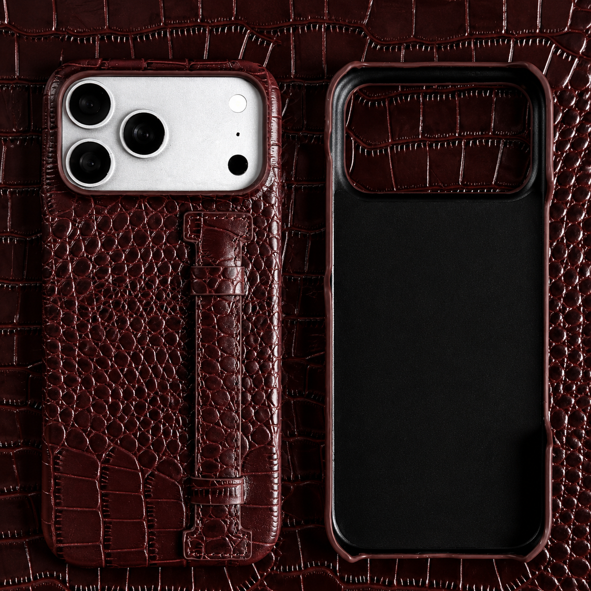 A dark brown crocodile-style case and matching empty shell lie on brown patterned material. A stitched vertical strap sits beneath the broad camera panel.