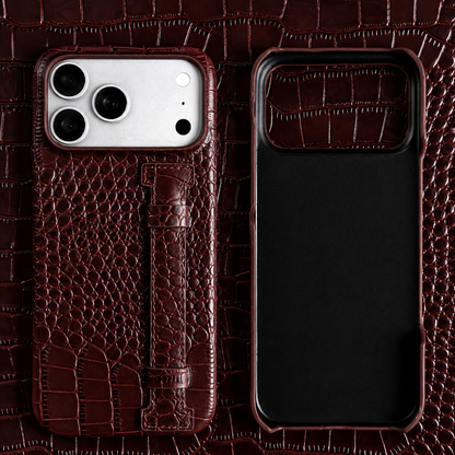 A dark brown crocodile-style case and matching empty shell lie on brown patterned material. A stitched vertical strap sits beneath the broad camera panel.