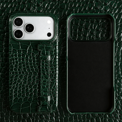 A dark green crocodile-style case and empty shell lie on matching patterned material. A narrow green back strap is secured by stitched end tabs.