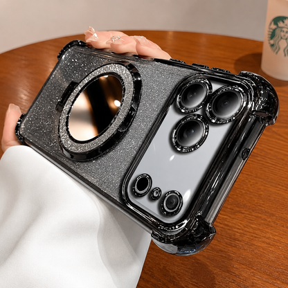 A hand in a white sleeve holds a black-trimmed silver glitter phone case horizontally above a wooden café table. A large round mirror with a sparkling border fills the back, and individual black rings surround the cameras in a silver-colored panel. A takeaway cup sits behind the hand.