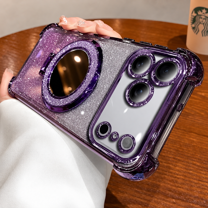 A hand holds a purple-trimmed silver glitter phone case horizontally above a wooden café table. A round mirror with a sparkling border fills the center of the back.