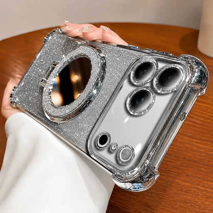 A hand holds a silver-trimmed glitter phone case horizontally above a wooden café table. A round mirror with a sparkling border sits beneath the raised camera panel.