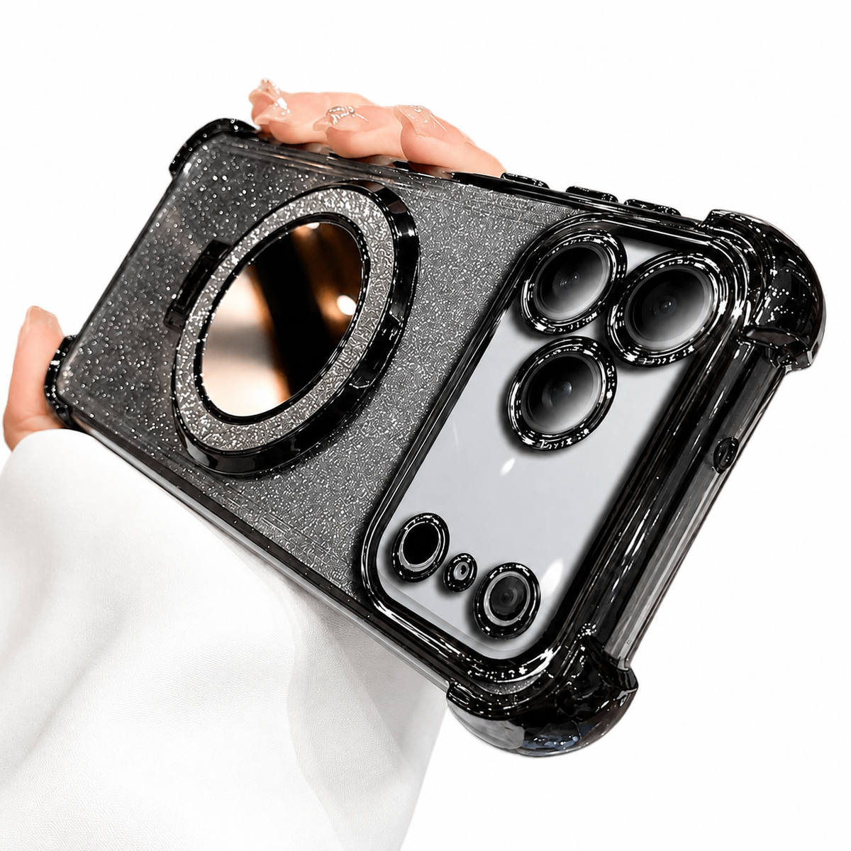 A hand holds a silver glitter phone case horizontally against a white background. Black reinforced corners frame the case, individual black rings surround the camera openings, and a large round mirror with a sparkling rim sits in the center.