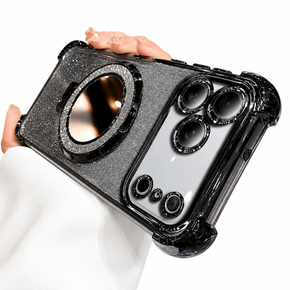 A hand holds a silver glitter phone case horizontally against a white background. Black reinforced corners frame the case, individual black rings surround the camera openings, and a large round mirror with a sparkling rim sits in the center.