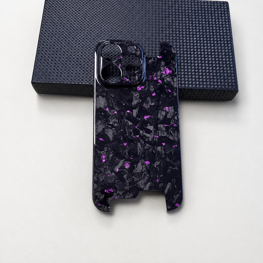 A glossy black phone case with purple and gray shard-like flecks rests beneath a dark textured box, showing circular camera openings and open sections at both ends.
