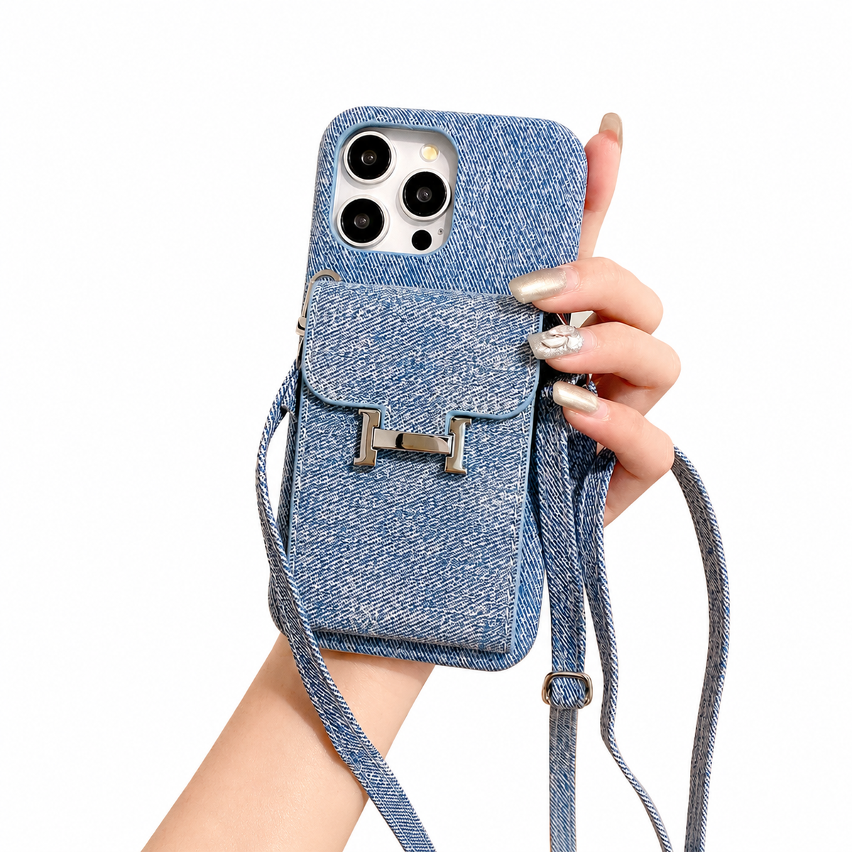 A hand holds a blue woven-textured case with a small flap pocket on its back. A silver H-shaped clasp closes the pocket, and matching long and short straps hang below.