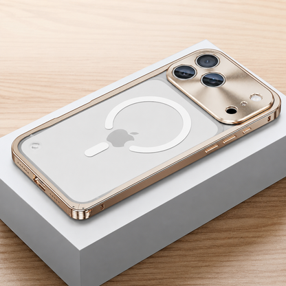 Gold-colored framed case lies face down on a white box, showing a frosted transparent back with a white broken magnetic ring and alignment bar. A broad reflective camera panel surrounds three lenses.