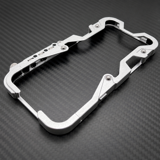 An empty silver bumper frame lies diagonally on a dark woven-patterned surface, showing its angular edges and exposed screws.
