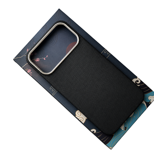 A black diagonal woven phone case rests on a blue illustrated box, showing its slim rounded edges and wide rectangular camera opening with silver-colored trim.