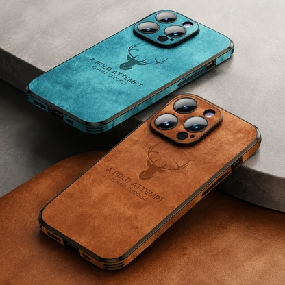 Turquoise and brown stag-design phone cases lie diagonally on pale stone and brown material. Raised surrounds frame three camera lenses, while motivational words appear across the textured backs.
