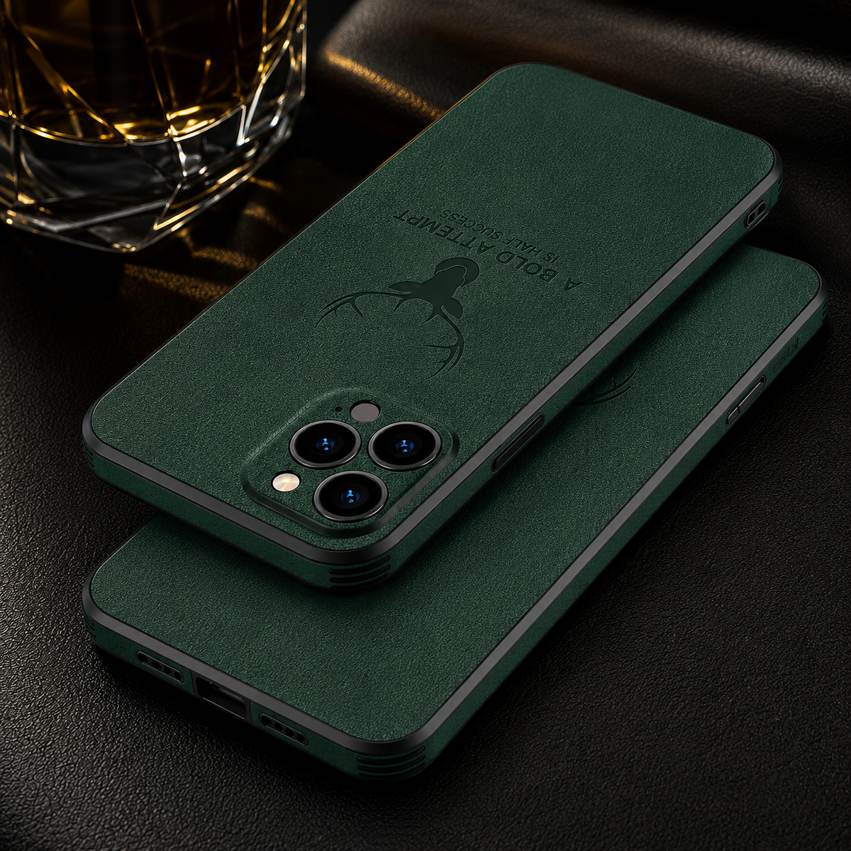 Two green textured cases overlap on a dark surface beside a glass, showing camera openings and embossed deer designs.